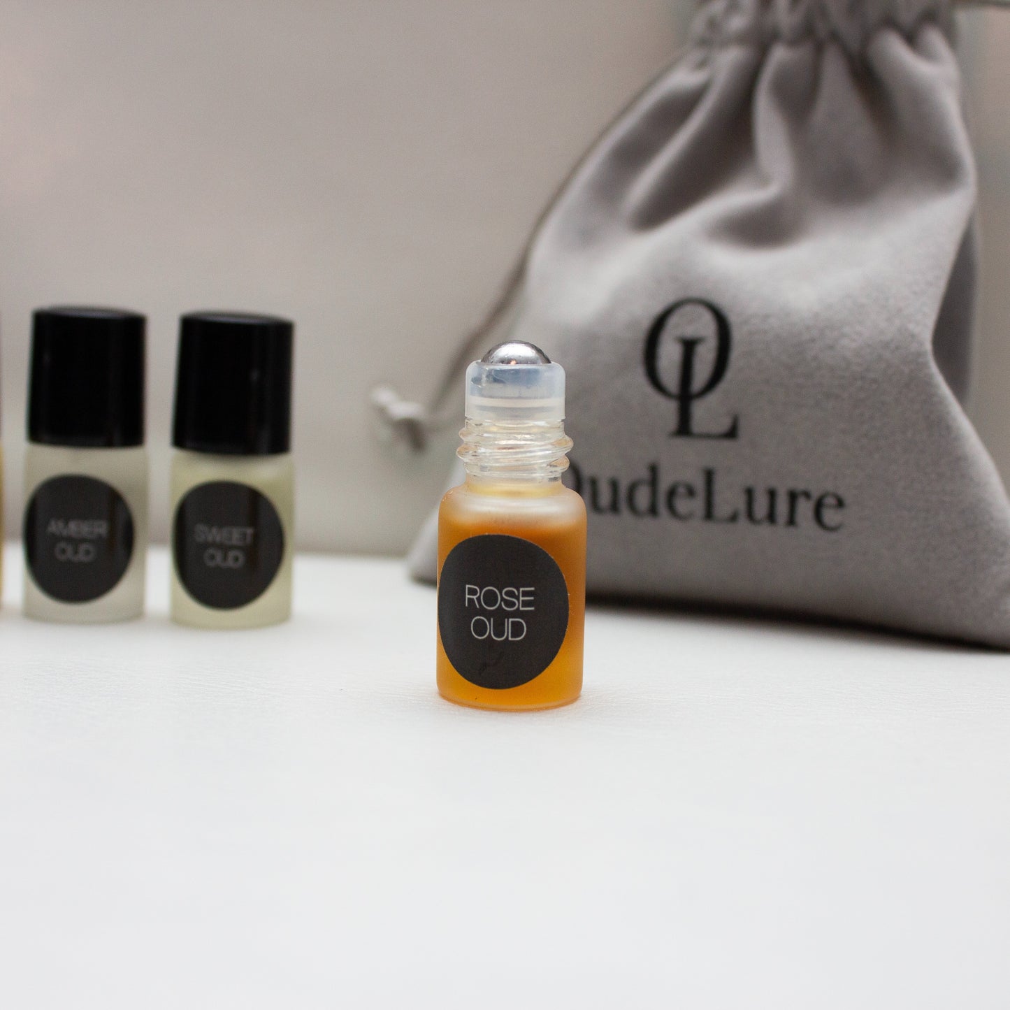 Small bottle of 'Rose Oud' with two other bottles and a branded pouch on a light surface.