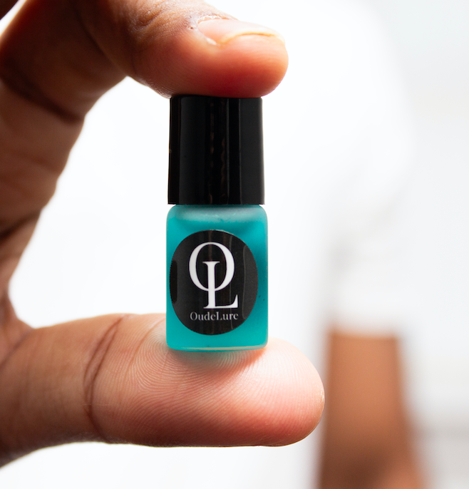 Small bottle of OudeLure held between fingers against a blurred background